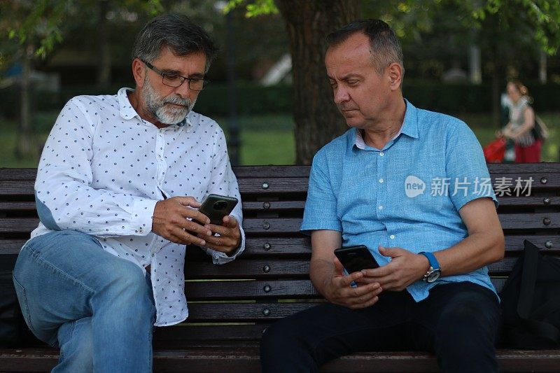 Two businessmen sitting on bench in public park
